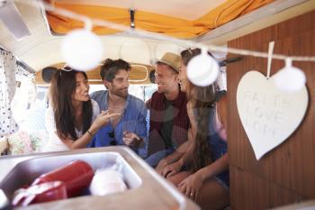 Four friends on a road trip talk in the back of a camper van