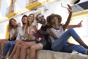 Five friends sitting on a wall in Ibiza taking a selfie