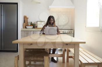 Young woman using laptop computer in her kitchen, front view