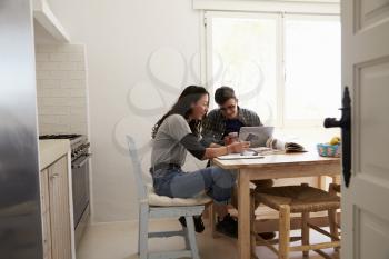 Two teenagers with laptop using smartphones at kitchen table