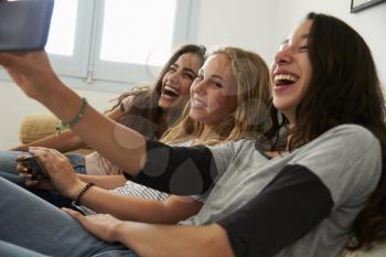 Teenage girl taking selfie with friends using her smartphone