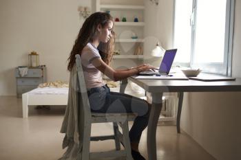 Girl using a laptop at a desk in her bedroom, full length