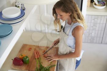 Woman standing in kitchen chopping vegetables, elevated view
