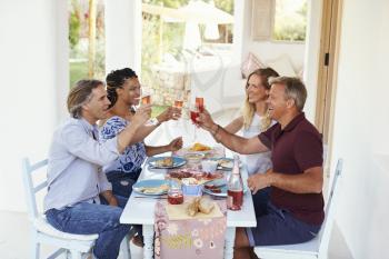 Two couples at a dinner table on a patio raise their glasses