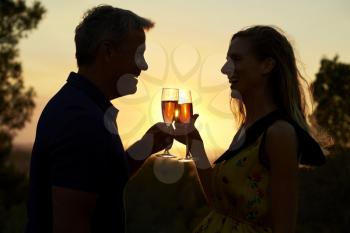 Romantic couple making a toast outdoors at sunset, waist up