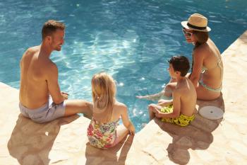 Rear View Of Family On Vacation Relaxing By Outdoor Pool