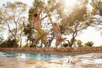 Rear View Of Children On Vacation Jumping Into Outdoor Pool