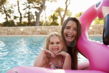 Mother And Daughter On Inflatables In Outdoor Swimming Pool