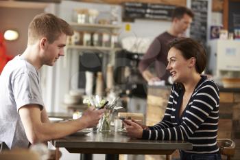Couple sitting in cafe using smartphones look at each other