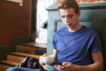 Man Sitting In Caf and Checking Messages On Mobile Phone