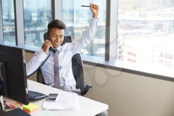 Celebrating Businessman Making Phone Call At Desk In Office