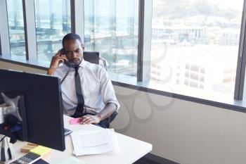 Businessman Making Phone Call Sitting At Desk In Office