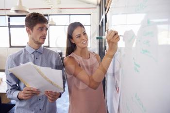 Young man and woman making notes on a whiteboard in office