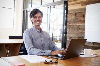 Mid-adult white man working in an office smiling to camera