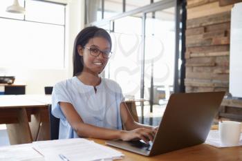 Young black woman using laptop in office smiling to camera