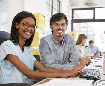 Man and young woman in open plan office looking to camera