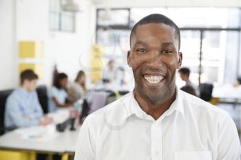Mid adult black man smiling to camera in an open plan office