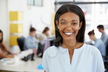 Young black woman smiling to camera in an open plan office