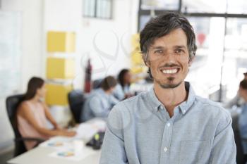 Mid adult white man smiling to camera in an open plan office