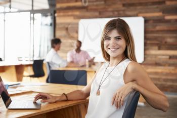Young white woman sitting in creative office looks to camera
