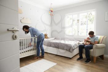 Mother Making Up Bed In Nursery Cot For Newborn Son