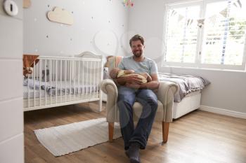 Father Sitting In Nursery Chair Holds Sleeping Baby Son