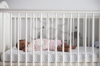 Side View Of Baby Girl Sleeping In Nursery Cot