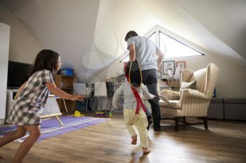 Father Having Game Of Tag With Children In Playroom