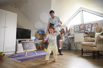 Father Having Game Of Tag With Children In Playroom