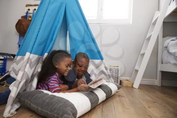 Two Children Lying In Tent In Playroom With Digital Tablet