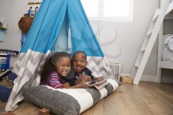 Two Children Lying In Tent In Playroom With Digital Tablet