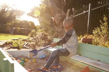 Boy Playing In Sand Box Outdoors In Garden