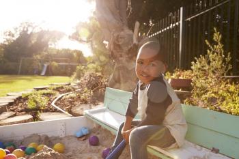 Portrait Of Boy Playing In Sand Box Outdoors In Garden