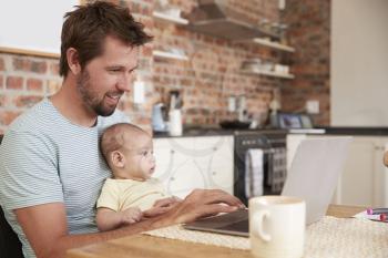 Father Working From Home On Laptop With Baby Son