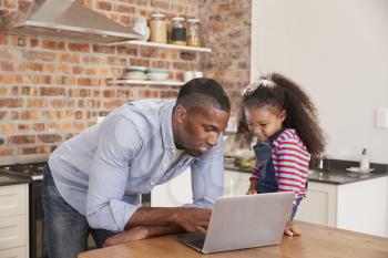 Father And Daughter Using Laptop In Kitchen At Home