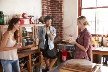 Three young adult girlfriends talk over coffee in kitchen