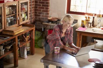Young woman using computer in kitchen, high angle