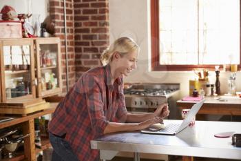 Young woman using computer in kitchen, waist up side view