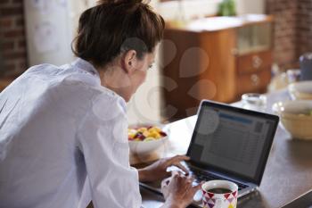 Young woman using laptop at breakfast, over shoulder view