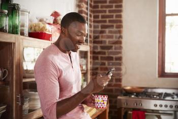 Young black man using smartphone in kitchen, close up
