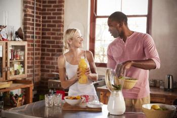 Mixed race couple making smoothies looking at each other