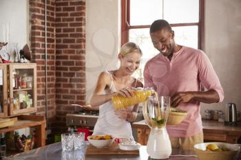 Happy mixed race couple making smoothies, pouring juice