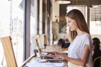Businesswoman By Window Working On Laptop In Coffee Shop