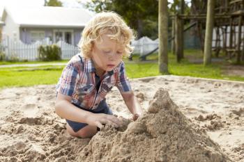 Male Pupil At Montessori School Playing In Sand Pit At Breaktime