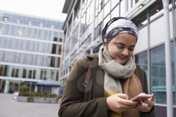 British Muslim Woman Texting On Mobile Phone Outside Office