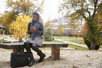 British Muslim Woman Texting On Mobile Phone In Park