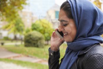 British Muslim Woman Using Mobile Phone In Park