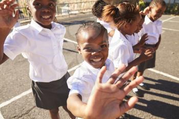 Young African schoolgirls in a playground waving to camera
