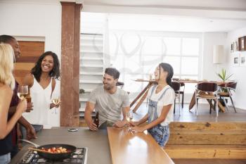 Friends Prepare And Serve Food For Dinner Party At Home Together