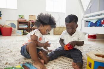 Baby Boy And Girl Playing With Toys In Playroom Together